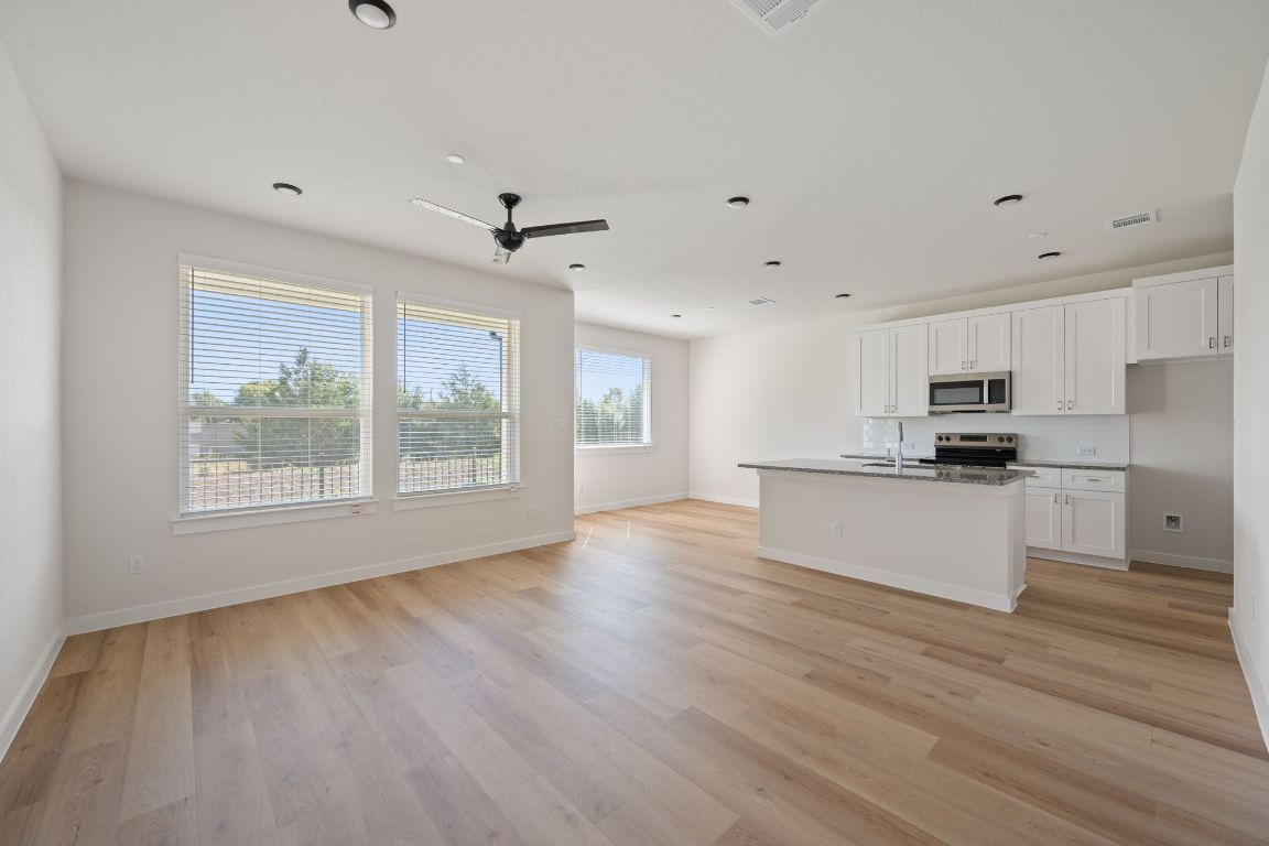 2600 Gattis School Road, Unit 1203 Round Rock, TX 78664 - Photo 25 of 25 Kitchen featuring white cabinets, open floor plan, an island with sink, appliances with stainless steel finishes, and light wood-style flooring
