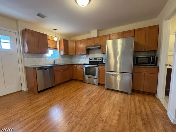 a kitchen with stainless steel appliances granite countertop a refrigerator a stove top oven a sink and dishwasher with wooden floor