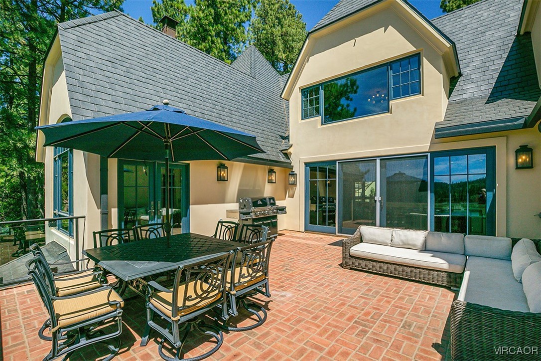28087 North Shore Road Lake Arrowhead, CA 92352 - Photo 35 of 48 a view of a patio with a dining table and chairs under an umbrella with a barbeque grill and a couch
