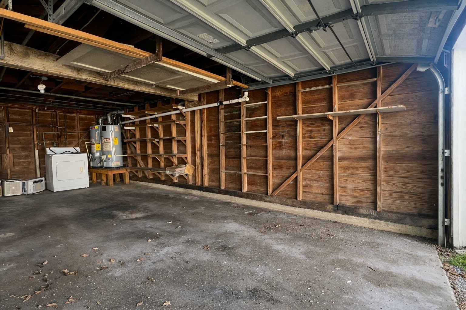 4917 Avenue R 1/2 Galveston, TX 77551 - Photo 19 of 21 Single-car garage interior with exposed wood framing, built-in shelving, concrete floor, water heater, and overhead garage door open to driveway.