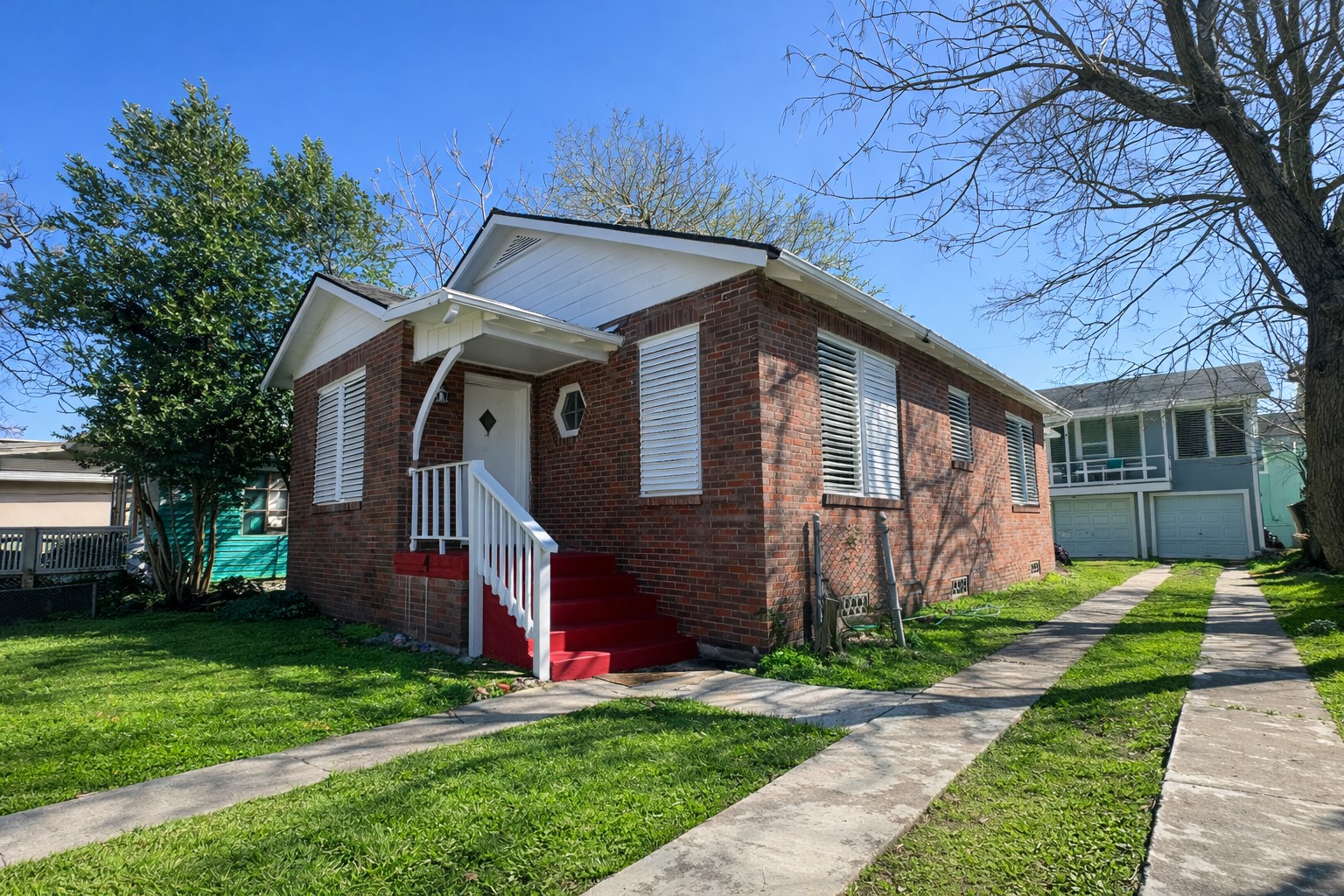 4917 Avenue R 1/2 Galveston, TX 77551 - Photo 4 of 21 Angled front view of single-story brick home with white shutters, red steps, concrete driveway strips, and neighboring homes in background.