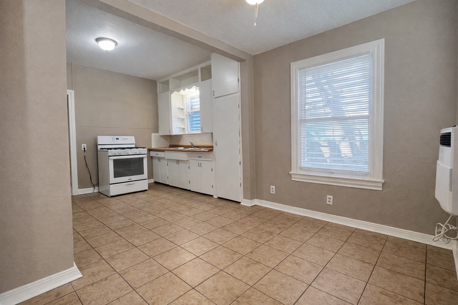 4917 Avenue R 1/2 Galveston, TX 77551 - Photo 8 of 21 Galveston TX kitchen with tile floors, white cabinetry, and natural light from exterior window.