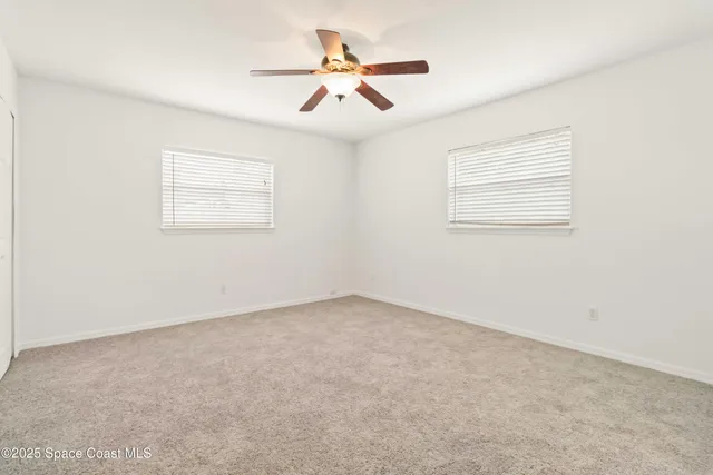 an empty room with ceiling fan and windows