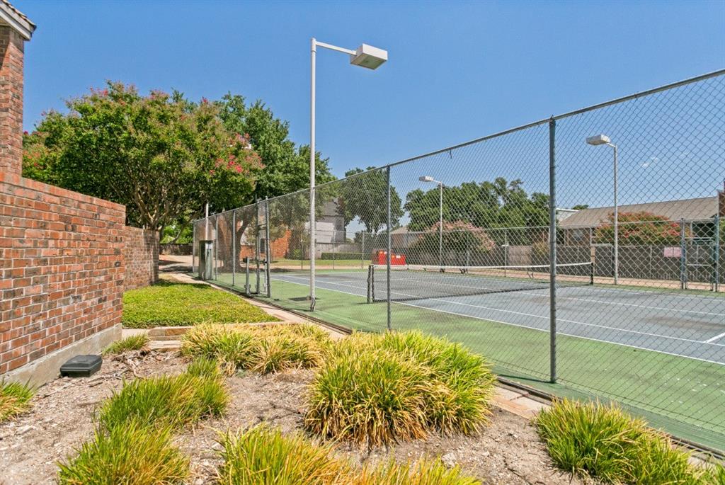 18240 Midway Road, Unit 905 Dallas, TX 75287 - Photo 9 of 29 Tennis court with chain-link fencing, featuring overhead lighting fixtures and a brick wall perimeter