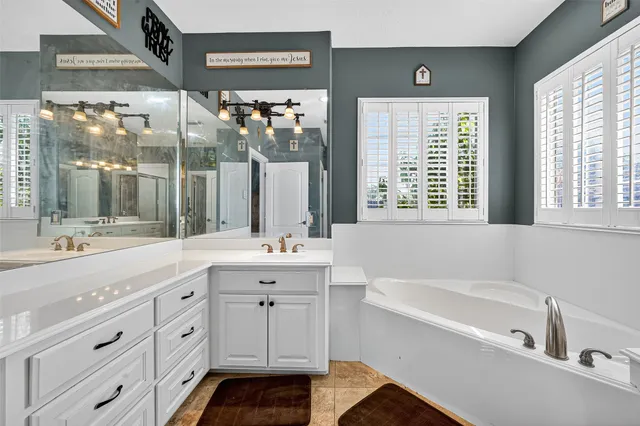 a spacious bathroom with a double vanity sink a mirror a bathtub and next to a window
