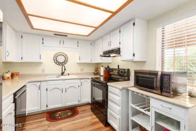 a kitchen with stainless steel appliances granite countertop a stove a sink dishwasher and white cabinets with wooden floor