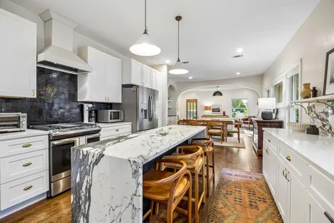 a open kitchen with stainless steel appliances granite countertop a stove top oven a sink a dining table and chairs with wooden floor