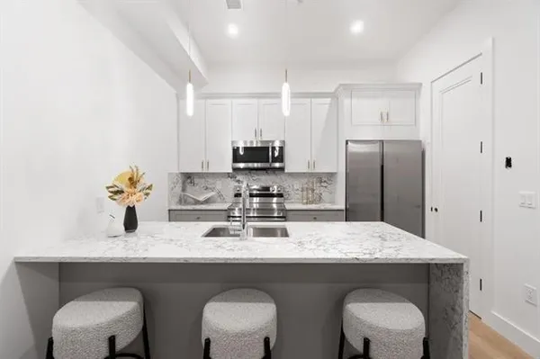 a kitchen with stainless steel appliances granite countertop a dining table chairs refrigerator and sink