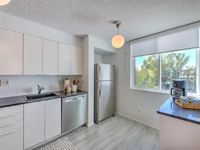 a kitchen with stainless steel appliances granite countertop a sink a refrigerator a stove and white cabinets with wooden floor