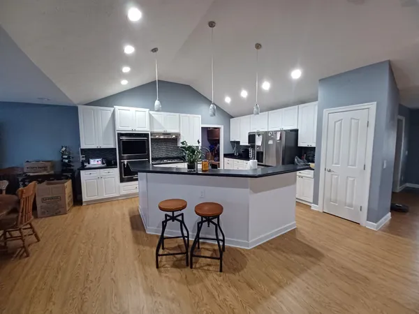 a kitchen with stainless steel appliances kitchen island granite countertop a refrigerator a stove a sink dishwasher and a dining table with wooden floor