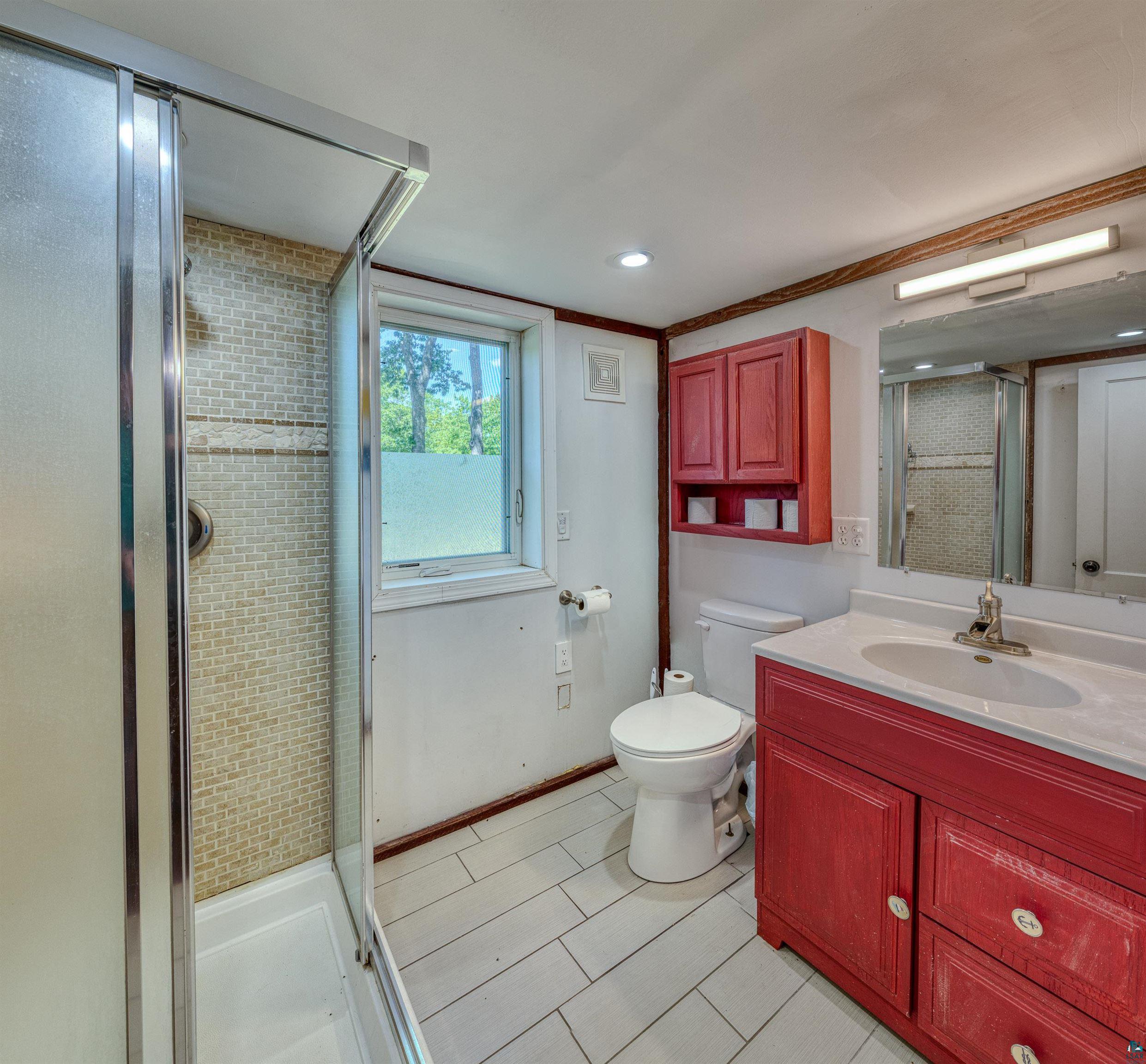 66075 Rooster Road Iron River, WI 54847 - Photo 12 of 52 Bathroom featuring a stand-up shower with mosaic tile surround, a single vanity with red cabinetry, and a window providing natural illumination