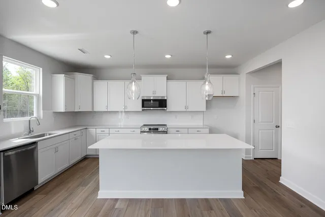 a large white kitchen with kitchen island a sink a center island stainless steel appliances and a window