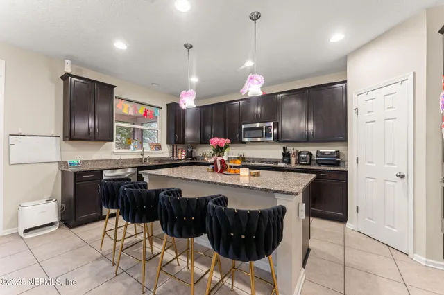 a kitchen with stainless steel appliances kitchen island granite countertop a sink a stove a refrigerator cabinets and chairs