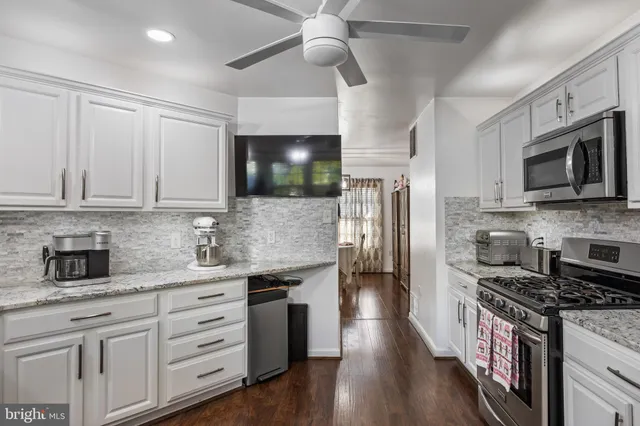 a kitchen with stainless steel appliances white cabinets a sink a stove a refrigerator and island with wooden floor