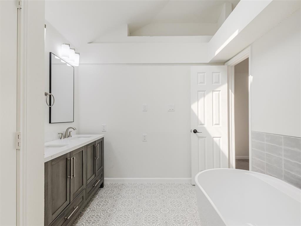 2327 North Ridge Road McKinney, TX 75072 - Photo 22 of 26 Dual vanity with undermount sinks, patterned floor tiling, freestanding soaking tub, and an accent wall with light gray rectangular tiles