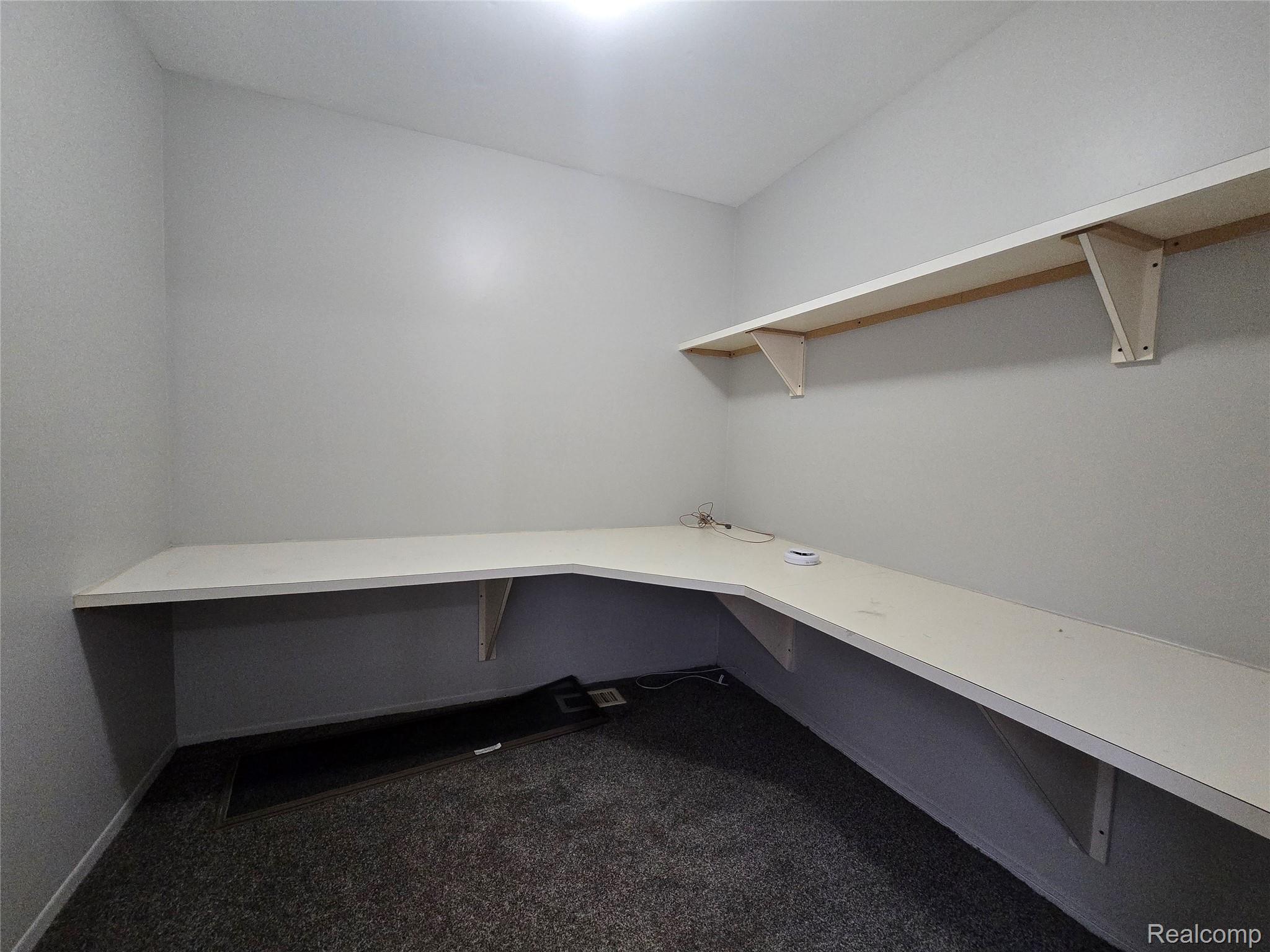 23568 Lahser Road Southfield, MI 48033 - Photo 11 of 18 Built-in corner desk with a white finish, complementary wall-mounted shelving, and textured gray carpeting