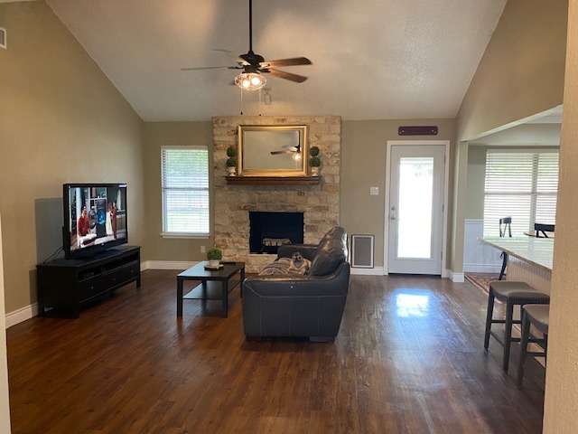 1002 Creekbend Cove Pflugerville, TX 78660 - Photo 12 of 16 Living area featuring a stone fireplace, lofted ceiling, dark wood-style flooring, and a ceiling fan