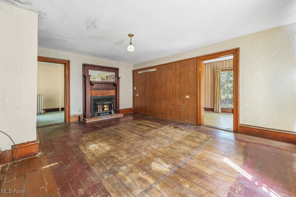 6727 Waterloo Road Atwater, OH 44201 - Photo 28 of 48 Unfurnished living room featuring dark wood finished floors, a fireplace, wallpapered walls, and radiator heating unit
