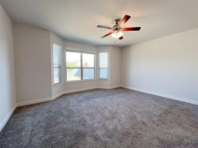 an empty room with chandelier fan and windows