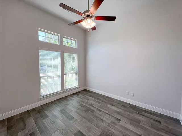 an empty room with wooden floor fan and windows