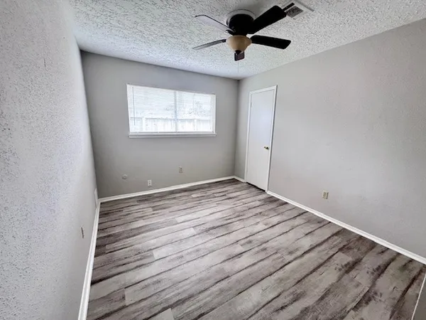 an empty room with wooden floor ceiling fan and windows