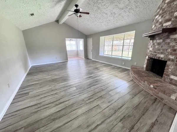 an empty room with wooden floor fireplace and windows