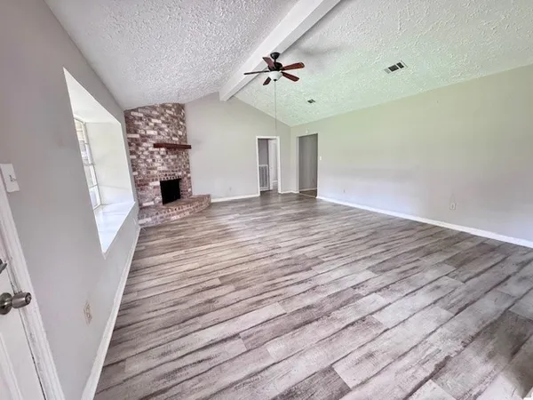 a view of an empty room with wooden floor and a fireplace
