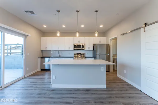 a view of kitchen with stainless steel appliances granite countertop a stove top oven a refrigerator and white cabinets with wooden floors