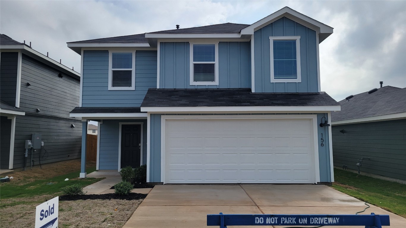 Traditional-style home featuring board and batten siding, roof with shingles, driveway, and an attached garage