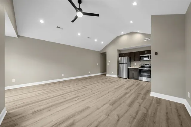 an empty room with wooden floor and kitchen view