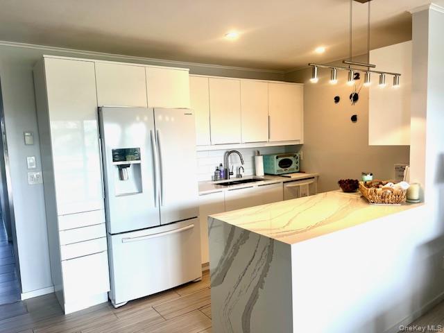 35 Library Avenue, Unit 6J Westhampton Beach, NY 11978 - Photo 11 of 19 Kitchen with refrigerator with ice dispenser, white cabinets, a peninsula, wood finish floors, and modern cabinets