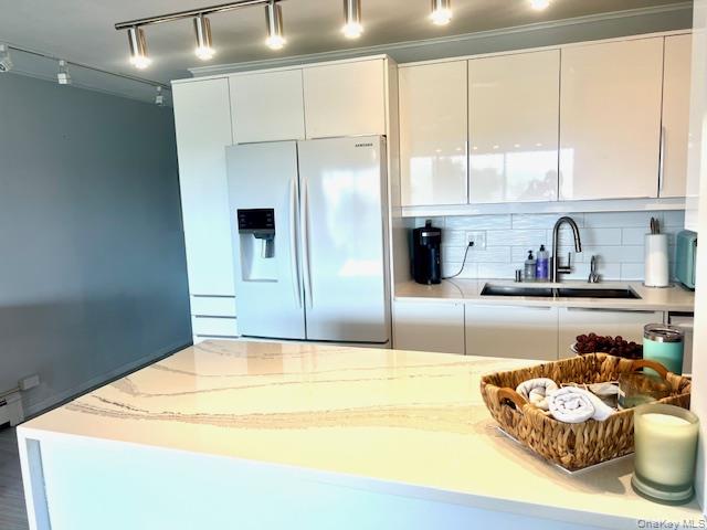 35 Library Avenue, Unit 6J Westhampton Beach, NY 11978 - Photo 12 of 19 Kitchen featuring track lighting, refrigerator with ice dispenser, modern cabinets, light stone counters, and white cabinets