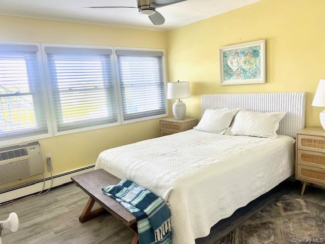 35 Library Avenue, Unit 6J Westhampton Beach, NY 11978 - Photo 6 of 19 Bedroom with wood finished floors, a baseboard heating unit, a ceiling fan, and an AC wall unit