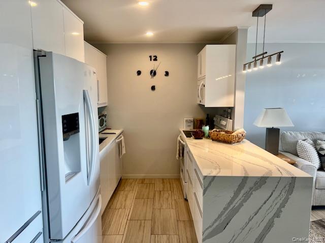 35 Library Avenue, Unit 6J Westhampton Beach, NY 11978 - Photo 10 of 19 Kitchen with white cabinets, light stone countertops, white appliances, decorative light fixtures, and a peninsula