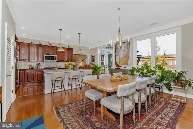 a kitchen with stainless steel appliances kitchen island granite countertop a refrigerator a stove top oven a dining table and chairs with wooden floor