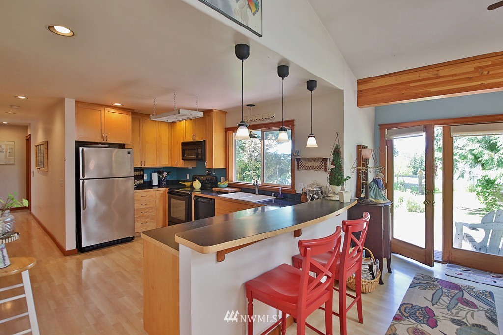 3608 East Harbor Road Langley, WA 98260 - Photo 9 of 25 a kitchen with stainless steel appliances granite countertop a refrigerator a sink dishwasher a stove and a dining table with wooden floor
