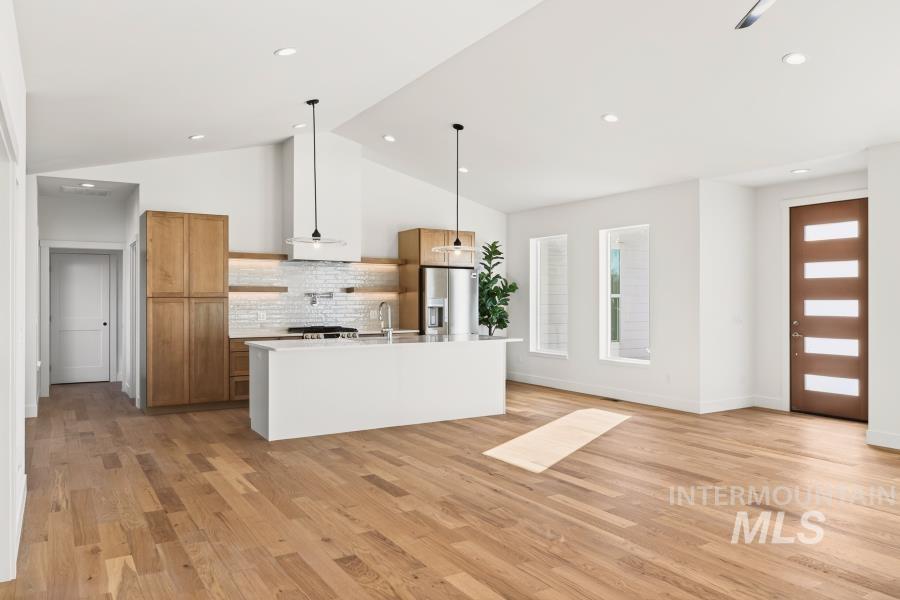 780 Victoria Drive Moscow, ID 83843 - Photo 15 of 44 Kitchen featuring decorative light fixtures, stainless steel fridge, an island with sink, light wood-type flooring, and vaulted ceiling