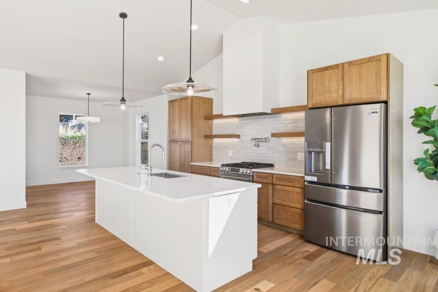780 Victoria Drive Moscow, ID 83843 - Photo 7 of 44 Two tone kitchen with stainless steel appliances, hanging light fixtures, lofted ceiling, a center island with sink, and light wood finished floors