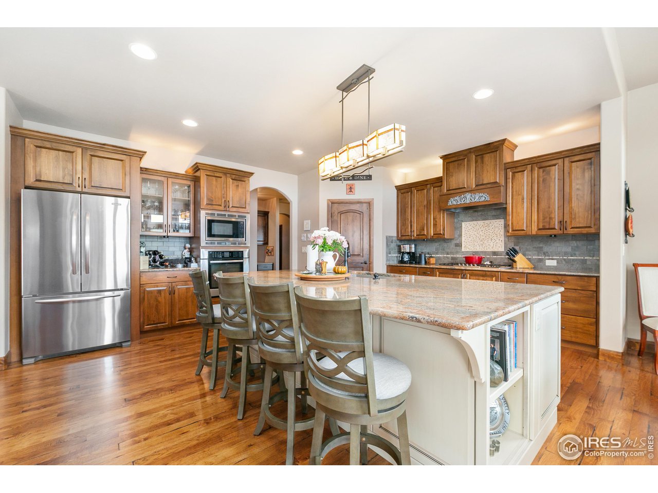a kitchen with stainless steel appliances kitchen island granite countertop a refrigerator a stove a sink a dining table and chairs with wooden floor