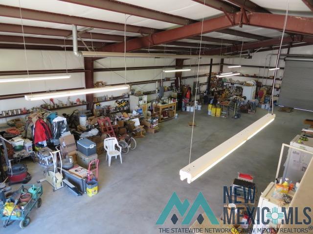 157 Mckinley Road Quemado, NM 87829 - Photo 9 of 10 Spacious warehouse interior featuring exposed metal beams, concrete flooring, fluorescent lighting, and a roll-up door