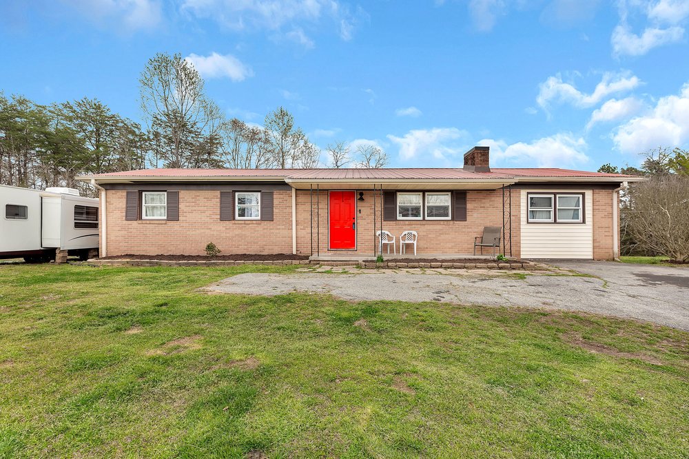 This ranch-style home features a vibrant red door, brick facade, and an expansive front and back yard.