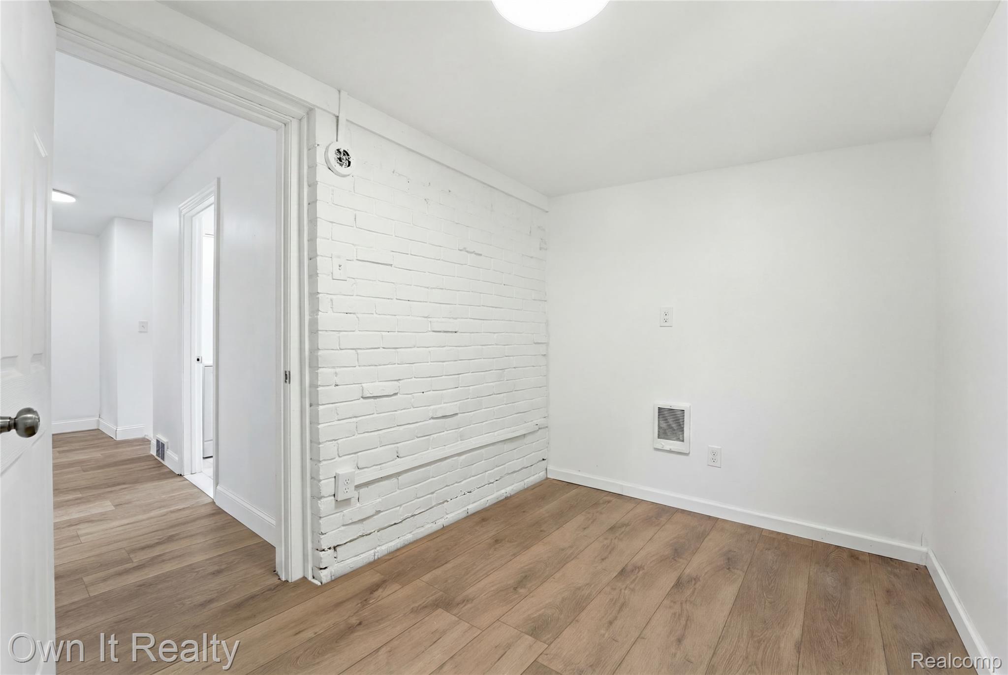 17351 Appoline Street Detroit, MI 48235 - Photo 18 of 34 Neutral interior featuring a white-painted exposed brick accent wall, wood-finish flooring, white baseboards, and a flush-mount ceiling light fixture