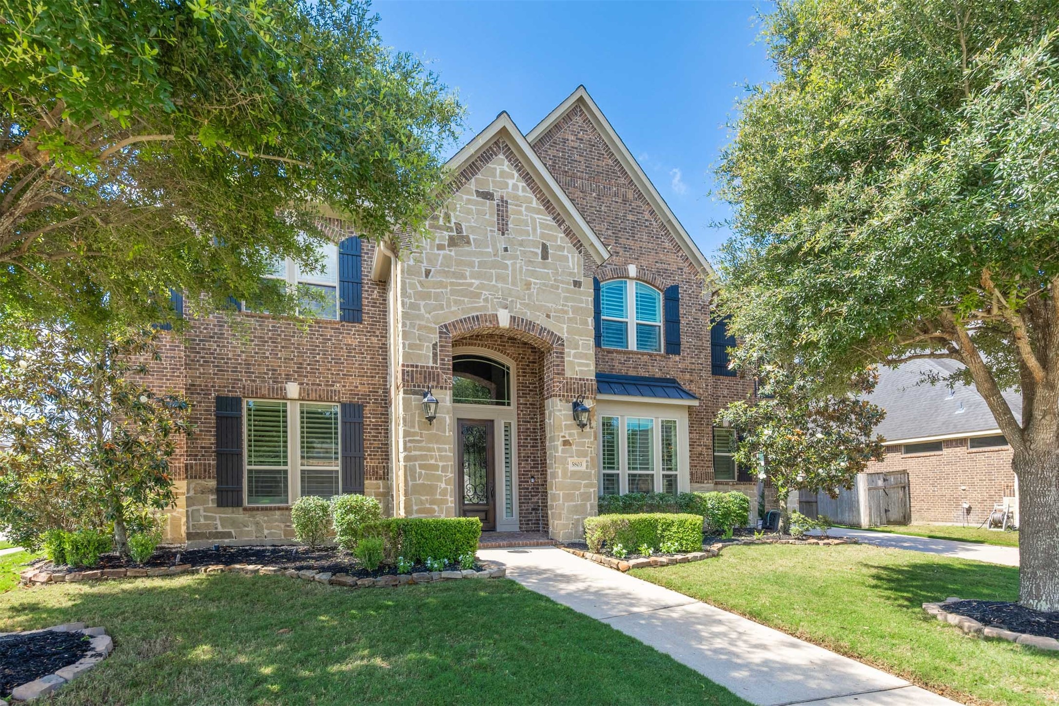 5803 Mustang Ridge Lane Fulshear, TX 77441 - Photo 47 of 48 Stunning brick and stone elevation is framed by mature trees and beautifully maintained landscaping, creating a warm and welcoming first impression. Arched architectural details, shutters and a grand covered entry add timeless character to the exterior design.