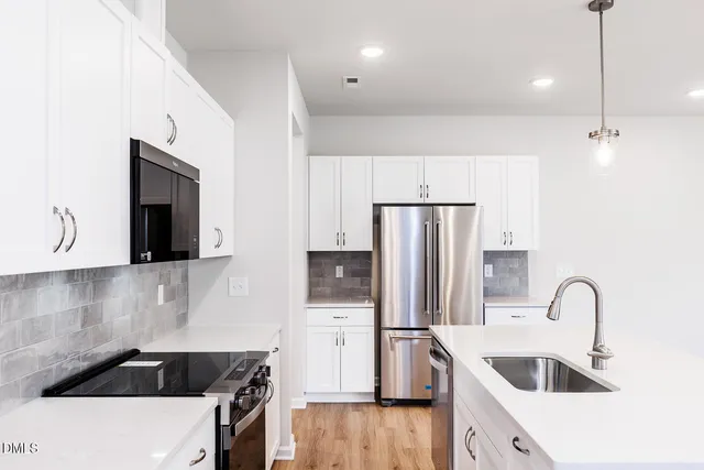 a kitchen with stainless steel appliances a refrigerator a sink a stove and white cabinets with wooden floor