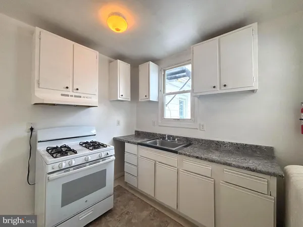 a kitchen with granite countertop white cabinets and a stove a sink with dishwasher