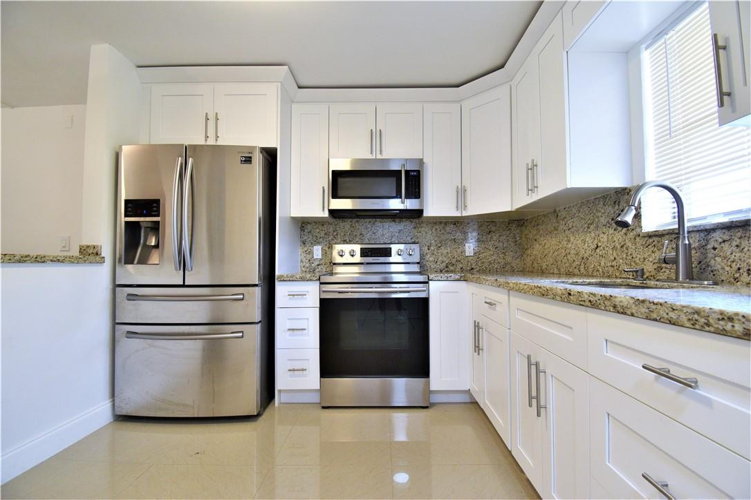 a kitchen with granite countertop a refrigerator stove and white cabinets