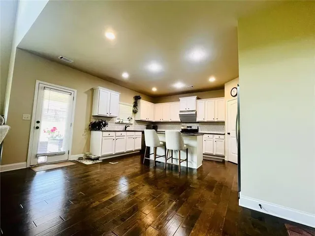 a kitchen with stainless steel appliances kitchen island granite countertop a refrigerator a stove and a dining table with wooden floor