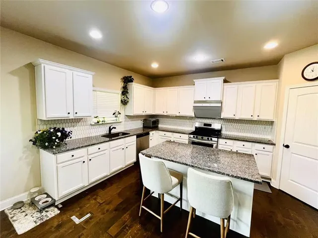 a kitchen with stainless steel appliances granite countertop a stove top oven a sink a refrigerator white cabinets and wooden floor