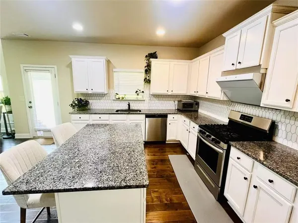 a large kitchen with stainless steel appliances granite countertop a stove a sink and a white cabinets
