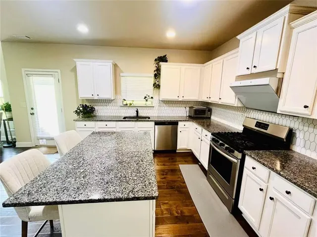 a large kitchen with stainless steel appliances granite countertop a stove a sink and a white cabinets